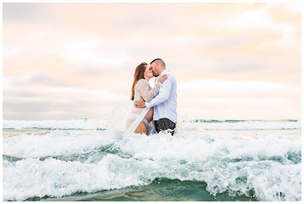 Maternity portrait of a couple kissing in the ocean in San Diego