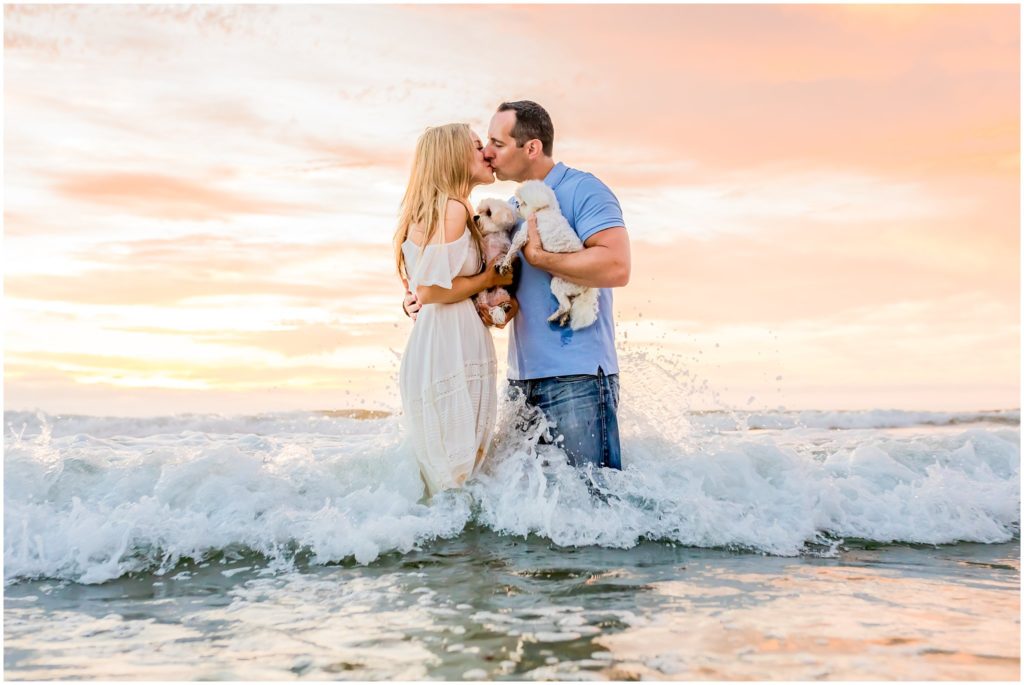 Couple kissing in the ocean and holding their puppies